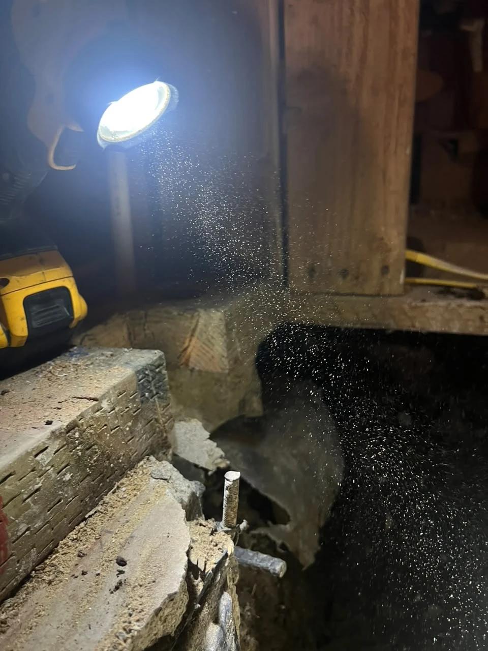 Fotografía de detalle de una lámpara de trabajo, estructura de madera, un borde de mampostería y polvo en suspensión