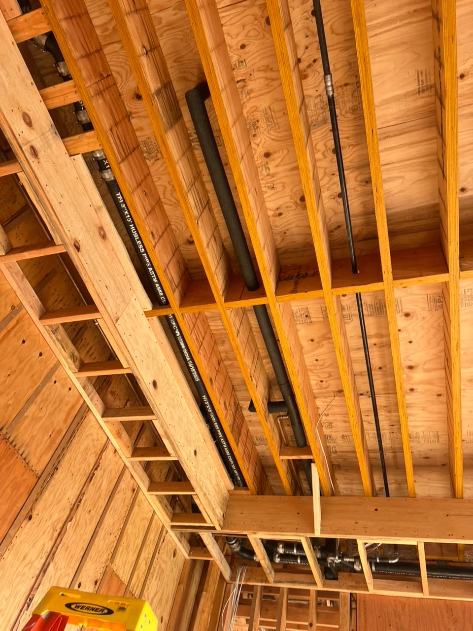 Fotografía de obra mirando hacia recorridos de tubería entre vigas de madera del techo
